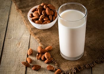 Tall glass of almond milk, sitting next to a small bowl of almonds on a table
